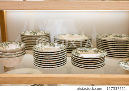 Elegant display of stacked vintage green and white ceramic plates on wooden shelves 137537551