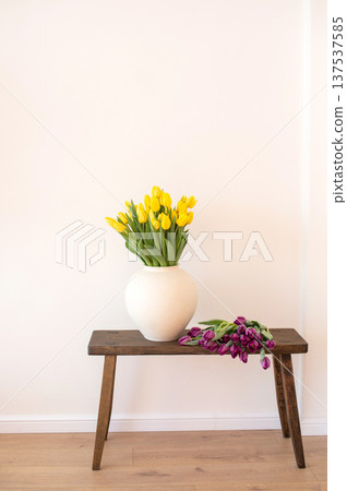 Yellow tulips in white vase on wooden bench against plain wall. Interior design Yellow tulips in white vase on wooden bench against plain wall. Interior design 137537585