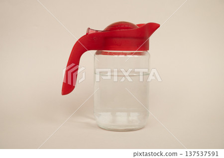 Clear glass syrup dispenser with red plastic lid on neutral background 137537591