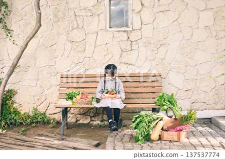 女孩坐在長椅上,旁邊放著蔬菜 女孩坐在長椅上,旁邊放著蔬菜 137537774