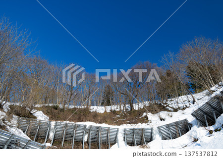 冬日景色,湛藍的天空,堅固的鋼製防護柵欄守護著白雪皚皚的山坡。 冬日景色,湛藍的天空,堅固的鋼製防護柵欄守護著白雪皚皚的山坡。 137537812