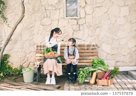 Parents and children sitting on a bench holding vegetables 137537879
