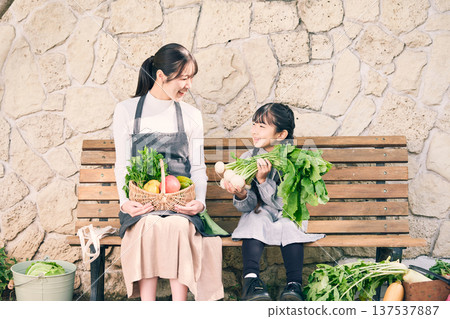 Parents and children sitting on a bench holding vegetables 137537887