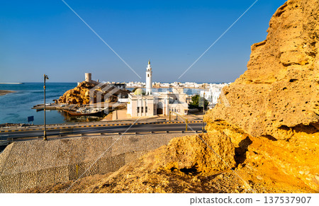 A scenic view of the mosque and Al Ayjah watchtowers along the waterfront in Sur, Oman, showcasing traditional architecture and a docked dhow boat. A scenic view of the mosque and Al Ayjah watchtowers along the waterfront in Sur, Oman, showcasing traditional architecture and a docked dhow boat. 137537907