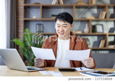 Happy asian man calculating budget and analyzing financial documents at home, paying bills while using laptop and planning his personal finance strategy for future savings Happy asian man calculating budget and analyzing financial documents at home, paying bills while using laptop and planning his personal finance strategy for future savings 137538608