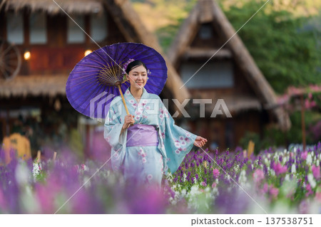 woman in yukata (kimono dress) holding umbrella with angelonia flower blooming in garden 137538751