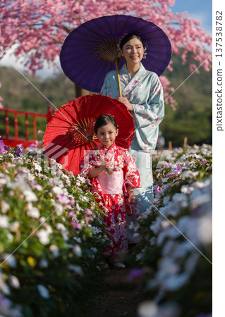 woman and child girl in yukata (kimono dress) with sakura flower or cherry blossom blooming in garden woman and child girl in yukata (kimono dress) with sakura flower or cherry blossom blooming in garden 137538782
