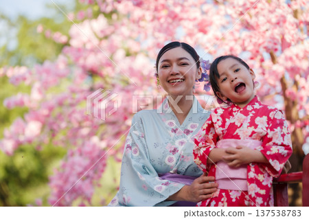woman and child girl in yukata (kimono dress) on red bridge with sakura flower or cherry blossom blooming in garden woman and child girl in yukata (kimono dress) on red bridge with sakura flower or cherry blossom blooming in garden 137538783
