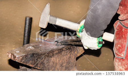 A blacksmith manually forges molten metal on an anvil in the forge A blacksmith manually forges molten metal on an anvil in the forge 137538963