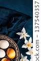 Easter eggs in basket with white daffodils on blue cloth background 137540357