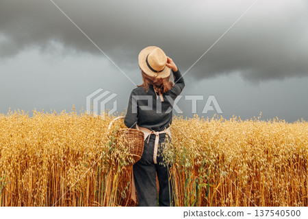 Girl in a wheat field wearing a straw hat on a cloudy day. Back view Girl in a wheat field wearing a straw hat on a cloudy day. Back view 137540500