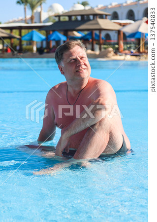 Happy overweight man sitting in the water of a shallow pool 137540833