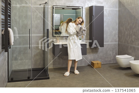 Happy woman standing in modern bathroom, wearing white bathrobe, slippers drying hair after shower Happy woman standing in modern bathroom, wearing white bathrobe, slippers drying hair after shower 137541065