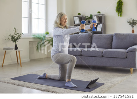 Senior older woman kneeling, holding dumbbells, exercising, workout, watching tablet online 137541581
