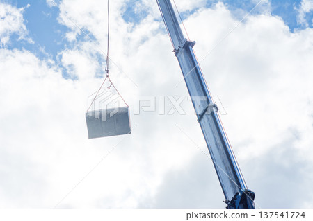 Heavy metal slab suspended from a crane against a cloudy sky at a construction site, showcasing the precision and effort in urban development and engineering challenges 137541724