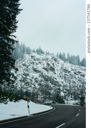 Winter road winding through snow-covered mountains under a gray sky, inviting adventure and exploration in a serene, tranquil landscape Winter road winding through snow-covered mountains under a gray sky, inviting adventure and exploration in a serene, tranquil landscape 137541766