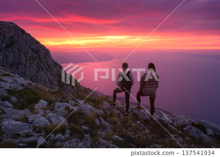 Two women hikers with backpacks standing on mountain at sunset 137541934