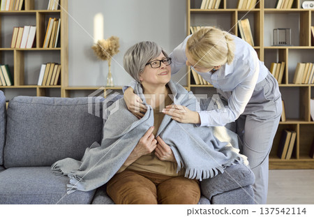 Senior woman wrapped in blanket with caregiver offering supportive home care Senior woman wrapped in blanket with caregiver offering supportive home care 137542114