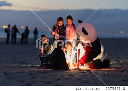 Children launching an illuminated lantern with panda costume on beach Children launching an illuminated lantern with panda costume on beach 137542140