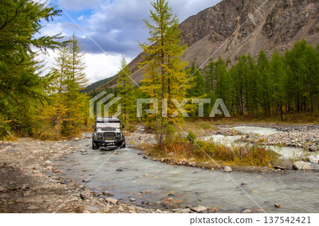 UAZ Hunter tourist SUV conquers a harsh mountain river Aktru flowing from glacier. Alpine camps and valley. Autumn sunny day. Landscape Mountains in Siberia. Chuiskiy Range, Altai Republic, Russia 137542421