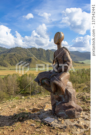 Monument of Children and Gopher in Mountains. Religious statue of the young bald thin man sitting on stone. Top of a mountain with golden face. Karakol. Uch-Enmek. Altai Republic. Ongudai, Russia. Monument of Children and Gopher in Mountains. Religious statue of the young bald thin man sitting on stone. Top of a mountain with golden face. Karakol. Uch-Enmek. Altai Republic. Ongudai, Russia. 137542441