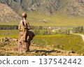 Monument of Children and Gopher in Mountains. Religious statue of the young bald thin man sitting on stone. Top of a mountain with golden face. Karakol. Uch-Enmek. Altai Republic. Ongudai, Russia. 137542442