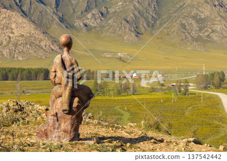 Monument of Children and Gopher in Mountains. Religious statue of the young bald thin man sitting on stone. Top of a mountain with golden face. Karakol. Uch-Enmek. Altai Republic. Ongudai, Russia. Monument of Children and Gopher in Mountains. Religious statue of the young bald thin man sitting on stone. Top of a mountain with golden face. Karakol. Uch-Enmek. Altai Republic. Ongudai, Russia. 137542442
