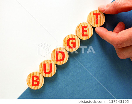 Budget symbol. Concept word Budget on beautiful wooden circles. Beautiful blue and white background. Businessman's hand. Business budget concept. Copy space. 137543105