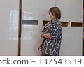 Young boy standing indoors with crossed arms. Caucasian child next to a glossy white wardrobe 137543539