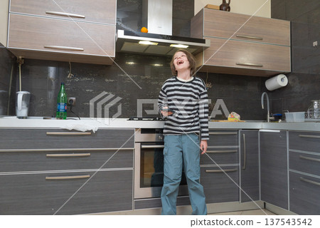 Laughing boy holding a smartphone in a modern kitchen. Happy child having fun with mobile device 137543542