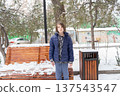 Young boy in a blue puffer jacket standing outdoors in a snowy park. Winter portrait of a child 137543547
