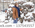 Young boy touching a snow-covered stone wall outdoors. Child exploring a winter urban environment 137543557