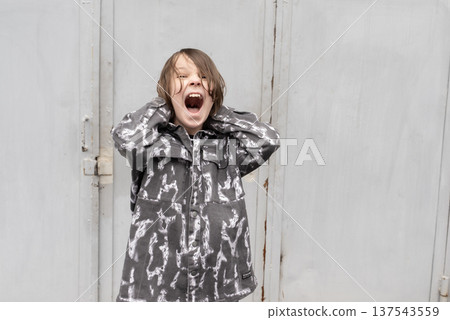Young boy screaming with hands on head. Frustrated child shouting outdoors against grey metal door Young boy screaming with hands on head. Frustrated child shouting outdoors against grey metal door 137543559