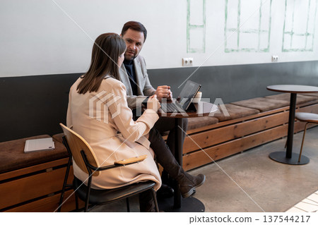 Business colleagues having a conversation at modern coffee shop table by window. Coffee shop, conversation, modern, business, teamwork. Business colleagues having a conversation at modern coffee shop table by window. Coffee shop, conversation, modern, business, teamwork. 137544217