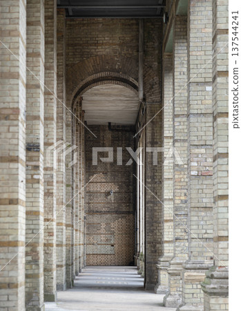 The arcade stretched out like a rhythmic countdown of stone and shadow. Each weathered pillar, stained with the pale gold of a low sun, stood as a silent witness to the years. The air felt heavy with 137544241