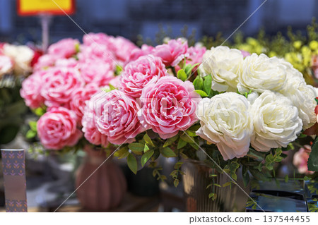 Artificial pink and white peonies in vases on a store counter. 137544455