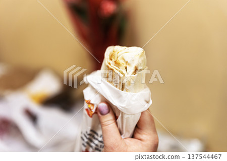 Close-up of a hand holding a freshly grilled chicken shawarma wrap. 137544467