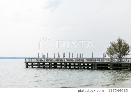 Wooden pier with lounge chairs and umbrellas on Lake Garda Wooden pier with lounge chairs and umbrellas on Lake Garda 137544685