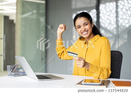 Young businesswoman smiling at laptop, celebrating successful online payment with credit card at modern office desk, excited about convenient e-commerce transaction and achievement Young businesswoman smiling at laptop, celebrating successful online payment with credit card at modern office desk, excited about convenient e-commerce transaction and achievement 137544820