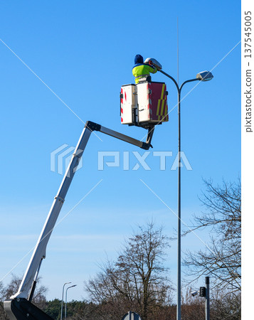 Worker Replacing Light Bulb in Street Lamp Using Hydraulic Lift on Clear Blue Sky Background 137545005