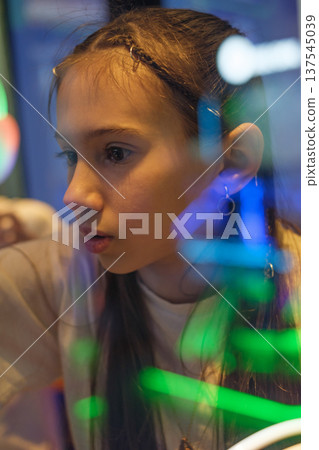 Close-up portrait of focused teenage girl illuminated by colorful neon lights in arcade. Emotional candid moment, concentration and modern youth lifestyle. Close-up portrait of focused teenage girl illuminated by colorful neon lights in arcade. Emotional candid moment, concentration and modern youth lifestyle. 137545039