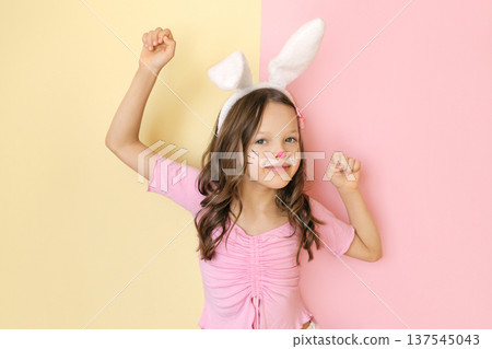 A cheerful dancing girl with rabbit ears and a painted face on a yellow-pink studio background. Celebration of the feast of Holy Easter A cheerful dancing girl with rabbit ears and a painted face on a yellow-pink studio background. Celebration of the feast of Holy Easter 137545043