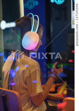A girl with headphones and a microphone in a karaoke booth at an amusement park is preparing for a performance A girl with headphones and a microphone in a karaoke booth at an amusement park is preparing for a performance 137545049