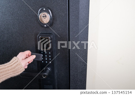 A woman opens a modern smart door lock using a contactless key. 137545154