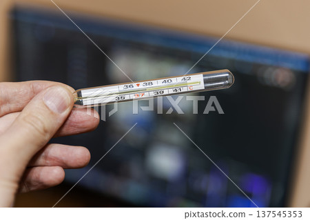 Hand holding a glass thermometer showing high body temperature. Hand holding a glass thermometer showing high body temperature. 137545353