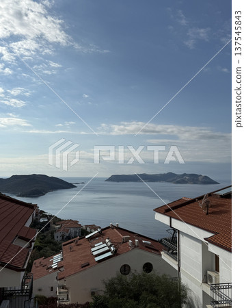 Coastal view with red roof houses, calm sea, and distant islands under a blue sky background 137545843
