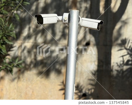 Surveillance cameras mounted on metal pole in outdoor setting with shadowed concrete background 137545845