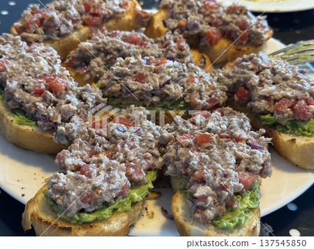 Tuna salad crostini with avocado spread and diced tomatoes on a white plate perfect for parties Tuna salad crostini with avocado spread and diced tomatoes on a white plate perfect for parties 137545850