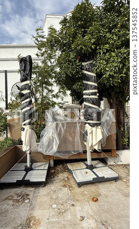 Outdoor patio umbrellas wrapped in protective covers beside orange tree background 137545852