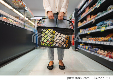 Woman shopping in grocery store aisle holding basket 137545987